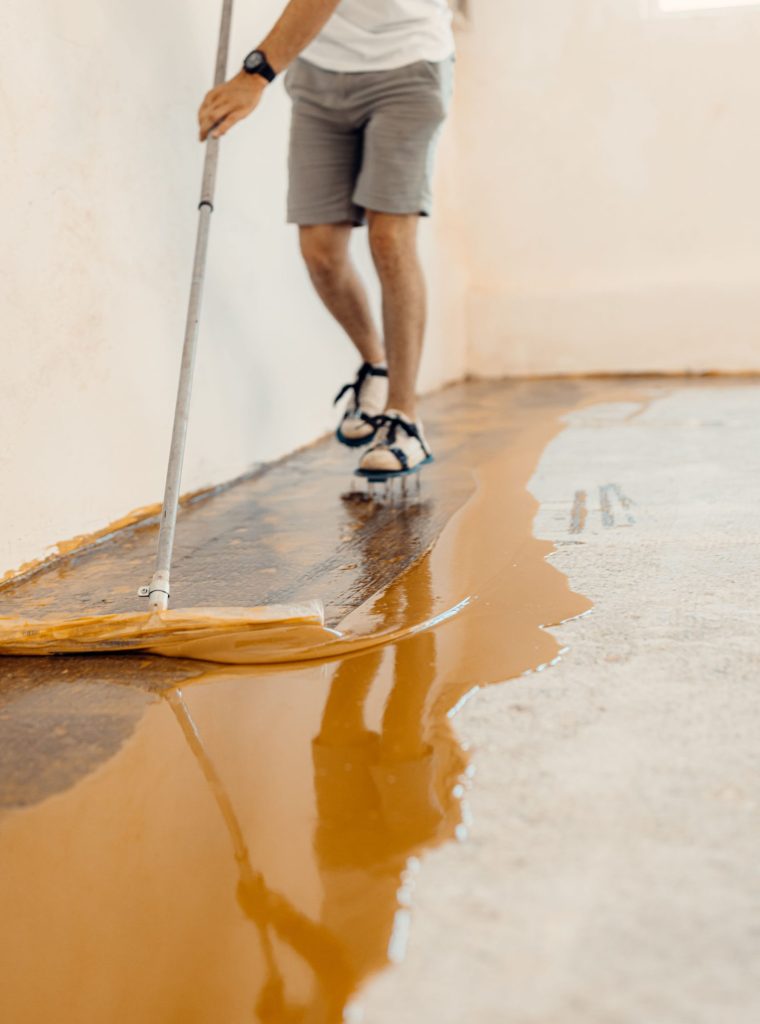 A closeup shot of a handyman applying yellow liquid paint on a new floor