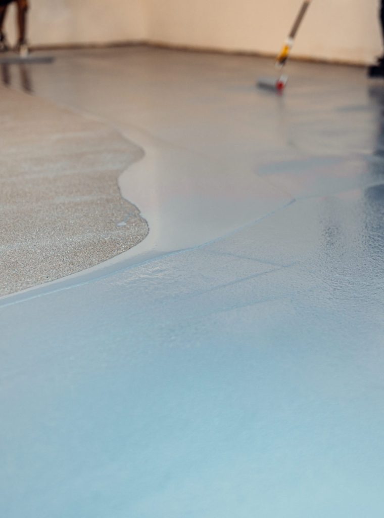 Workers applying epoxy flooring with trowel and paint roller